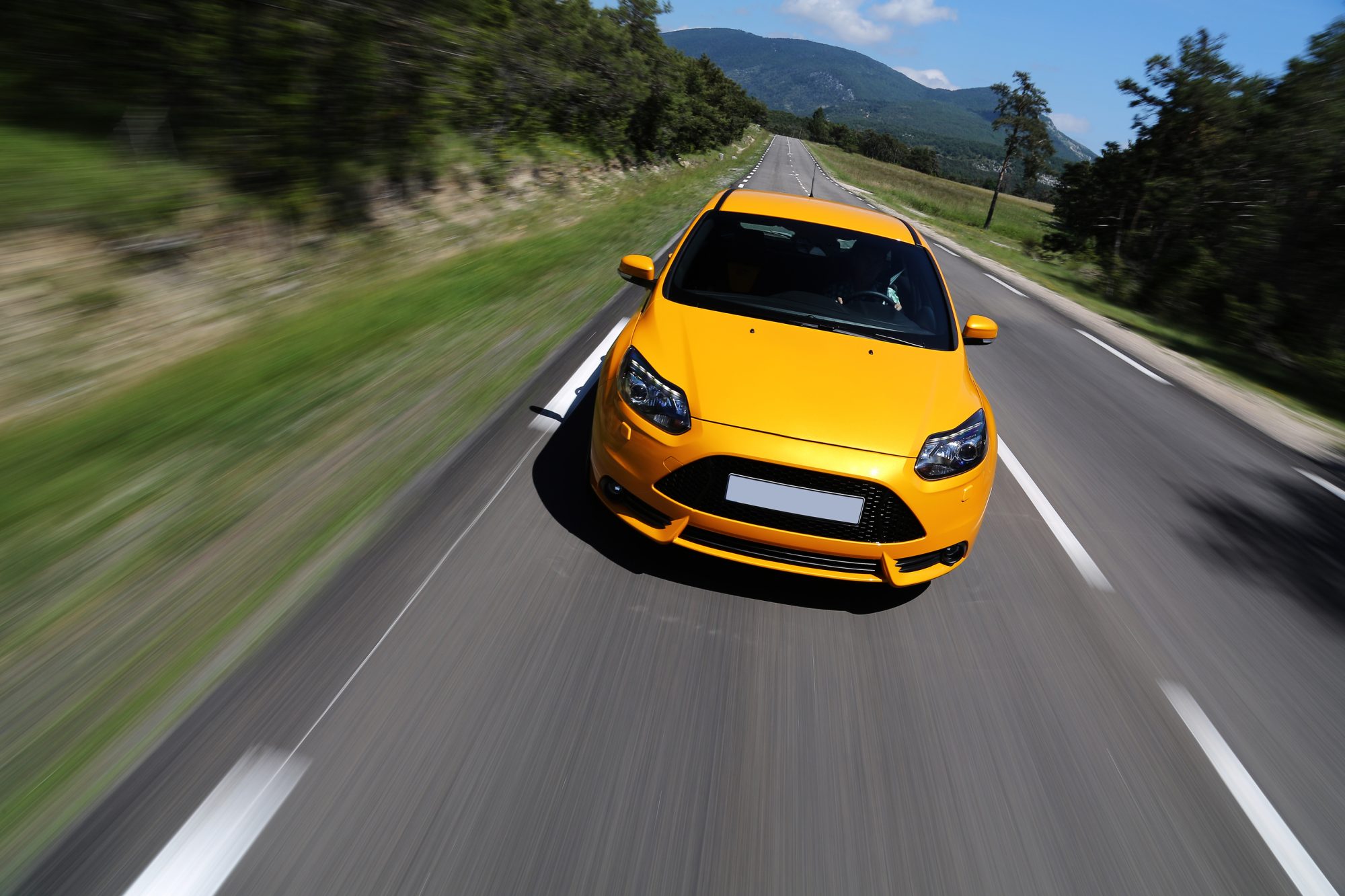 High angle shot of a yellow car driving fast down the road on a nice sunny day with some clouds on a blue sky